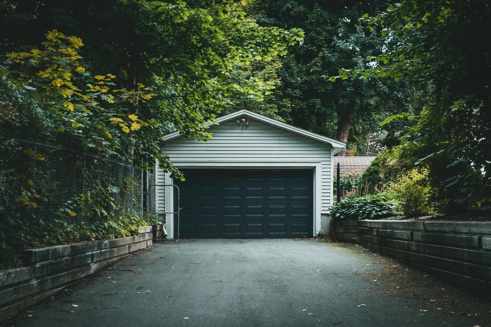 A detached garage with an anthracite sectional door at the end of a tree-lined drive