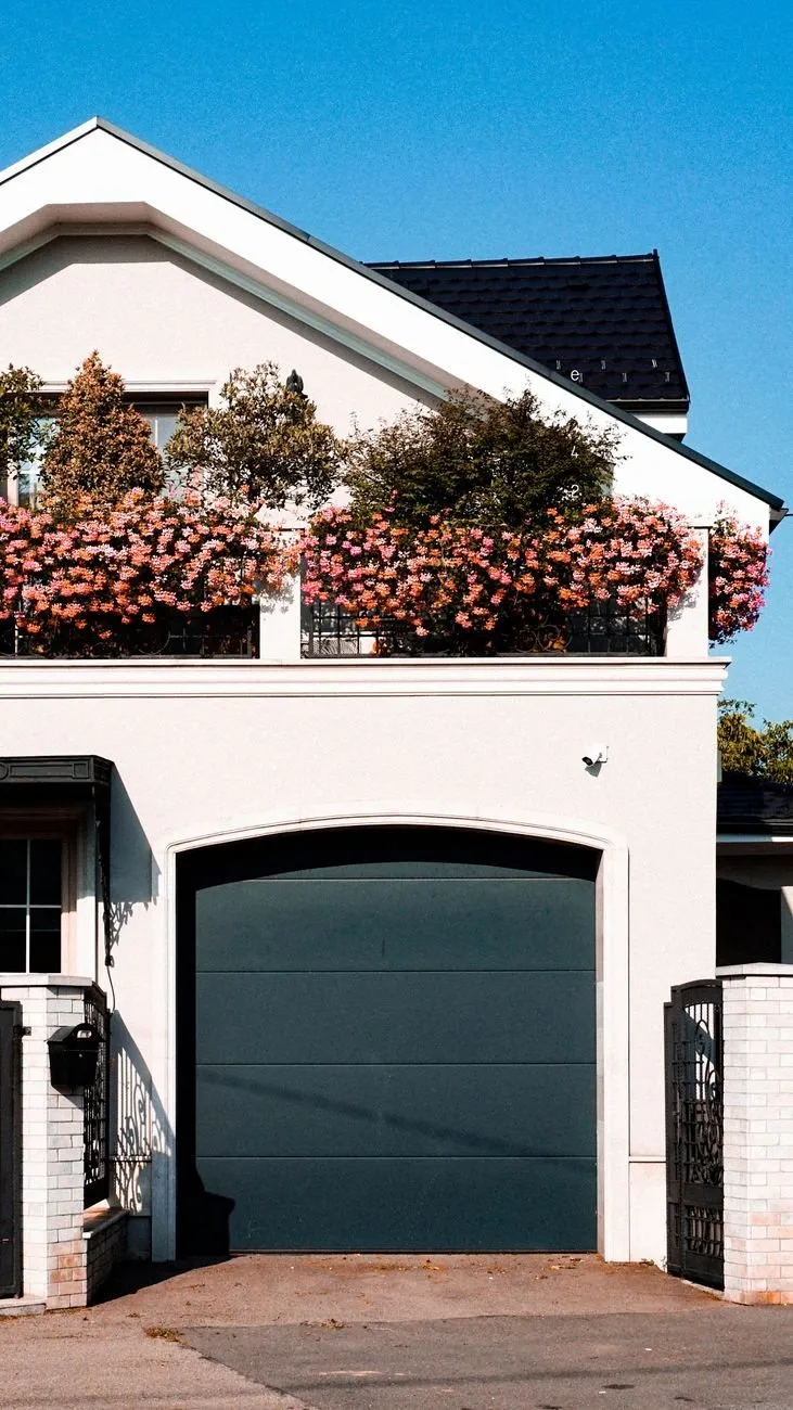 An anthracite sectional door in an arched opening under a balcony of pink geraniums