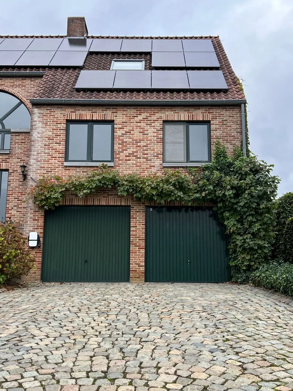Two dark green steel up-and-over doors in a red brick house with a cobbled drive