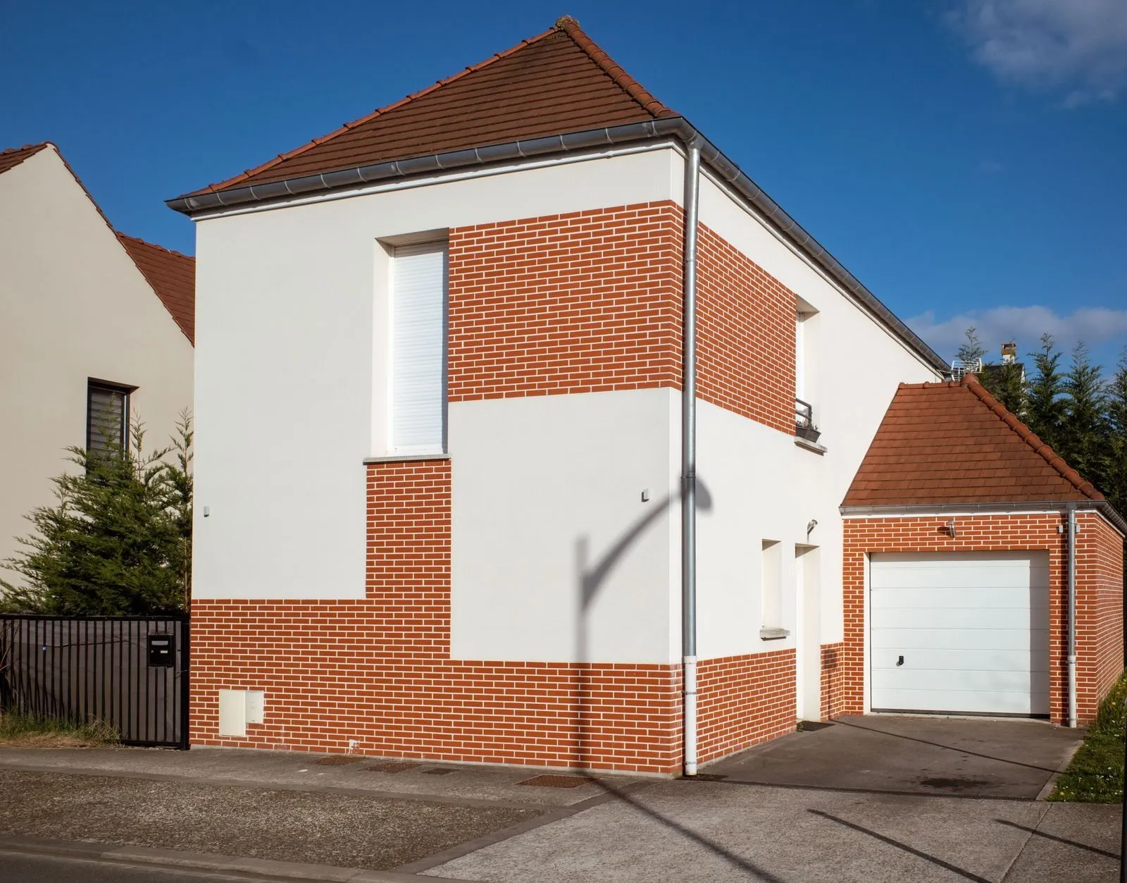 A white sectional garage door in a red brick garage beside a white rendered house under a blue sky