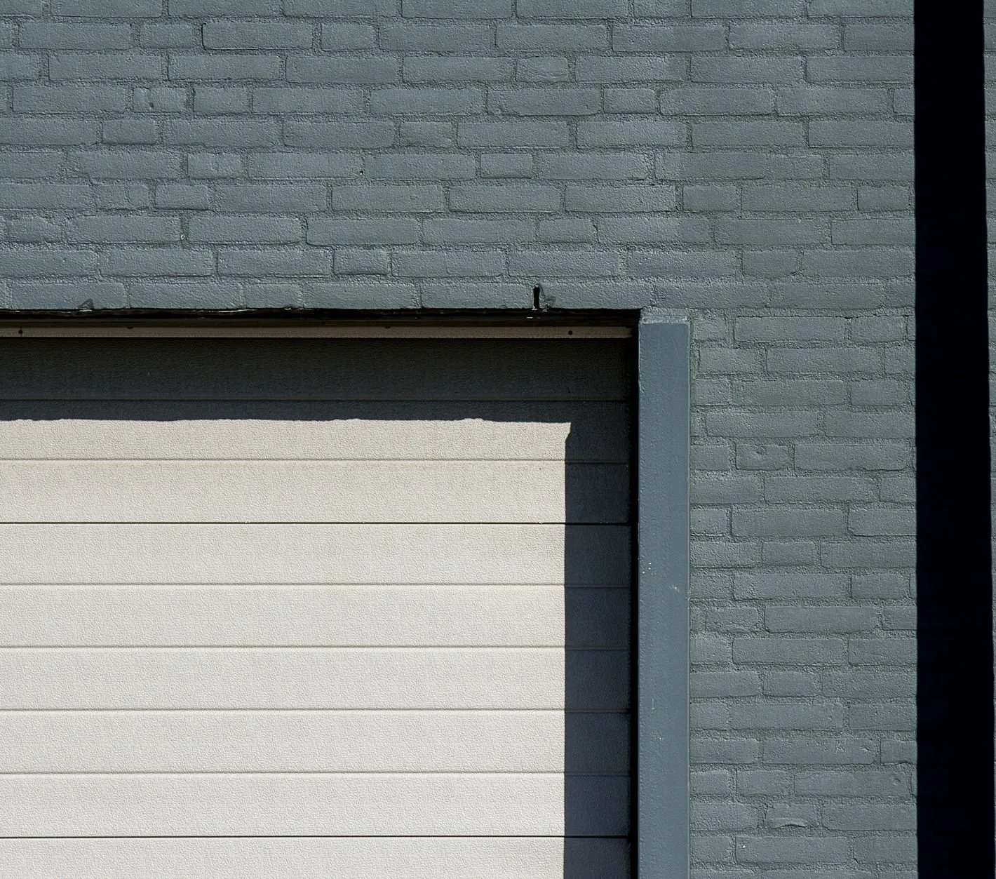 A light grey ribbed sectional door set in a painted grey brick wall