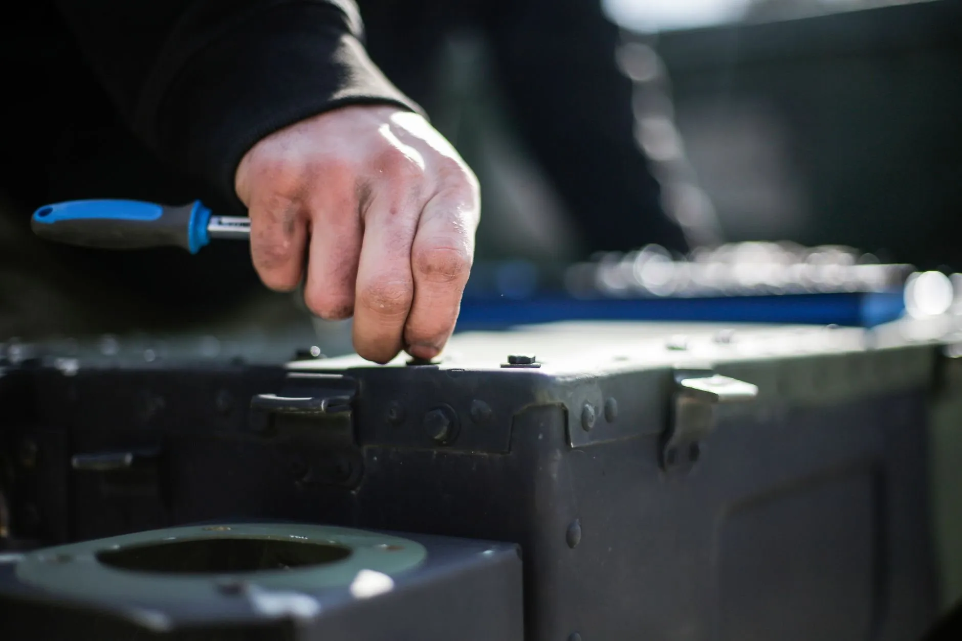 A hand turning a ratchet with a blue handle on a dark steel case