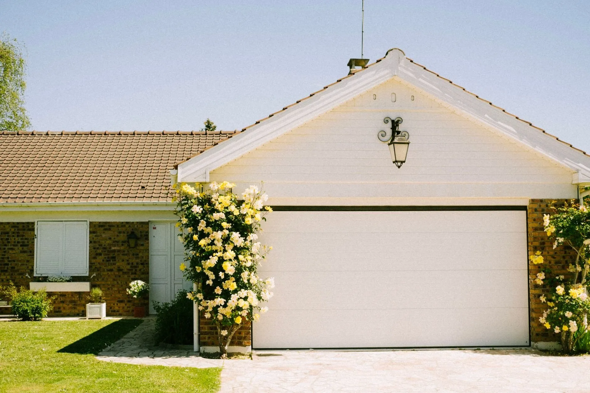 A bungalow with a cream sectional garage door framed by climbing yellow roses