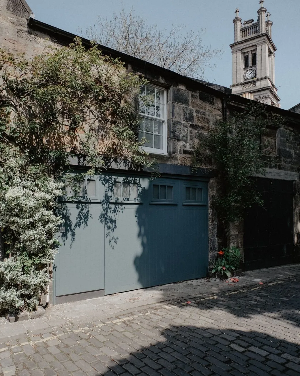 A grey-blue timber garage door in an old stone mews building with a clock tower behind