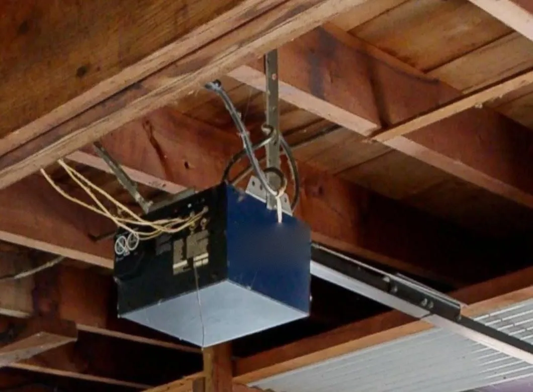 A garage door opener hanging from the ceiling joists, its drive rail running off towards the door
