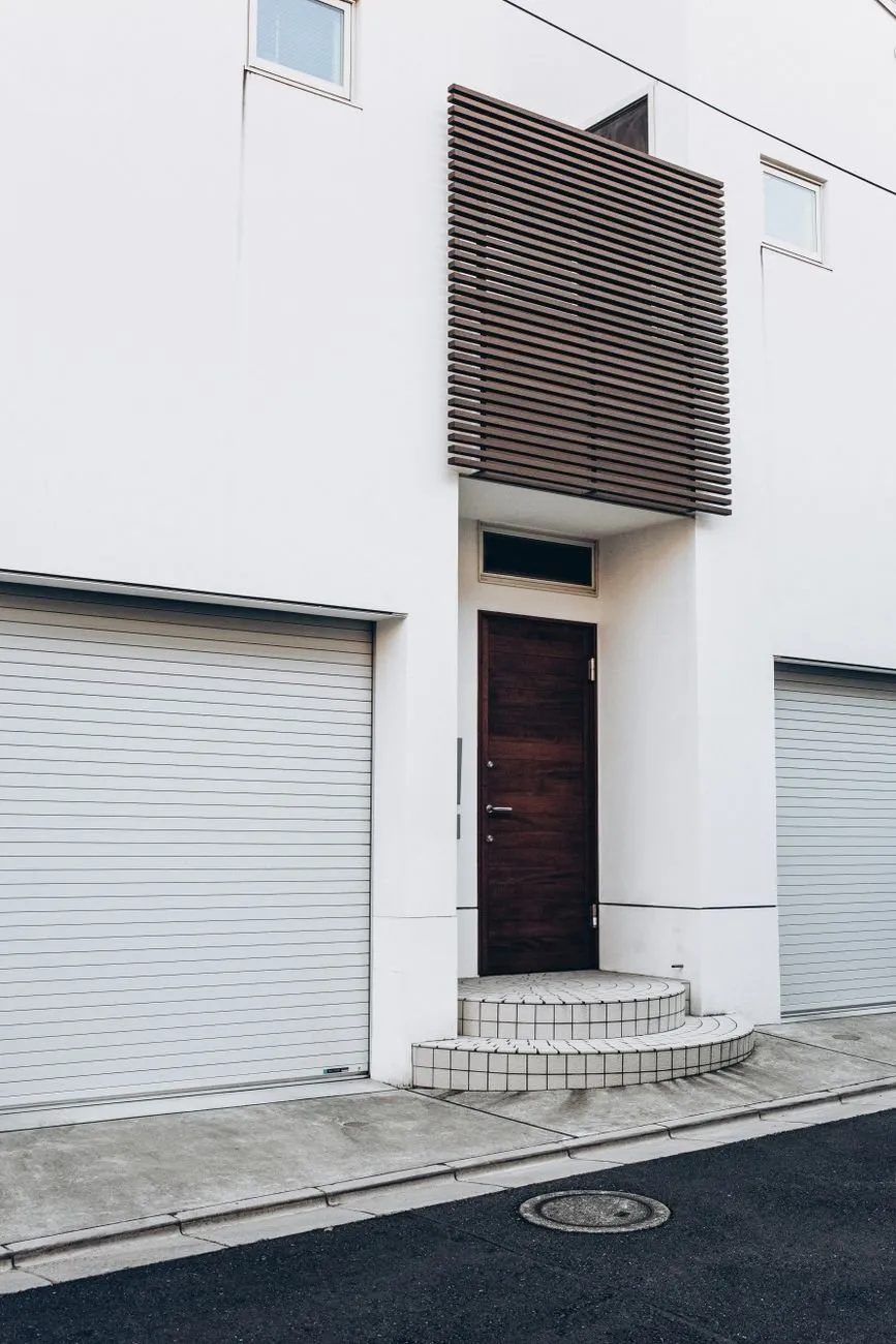 Two white aluminium roller doors either side of a front door on a white house