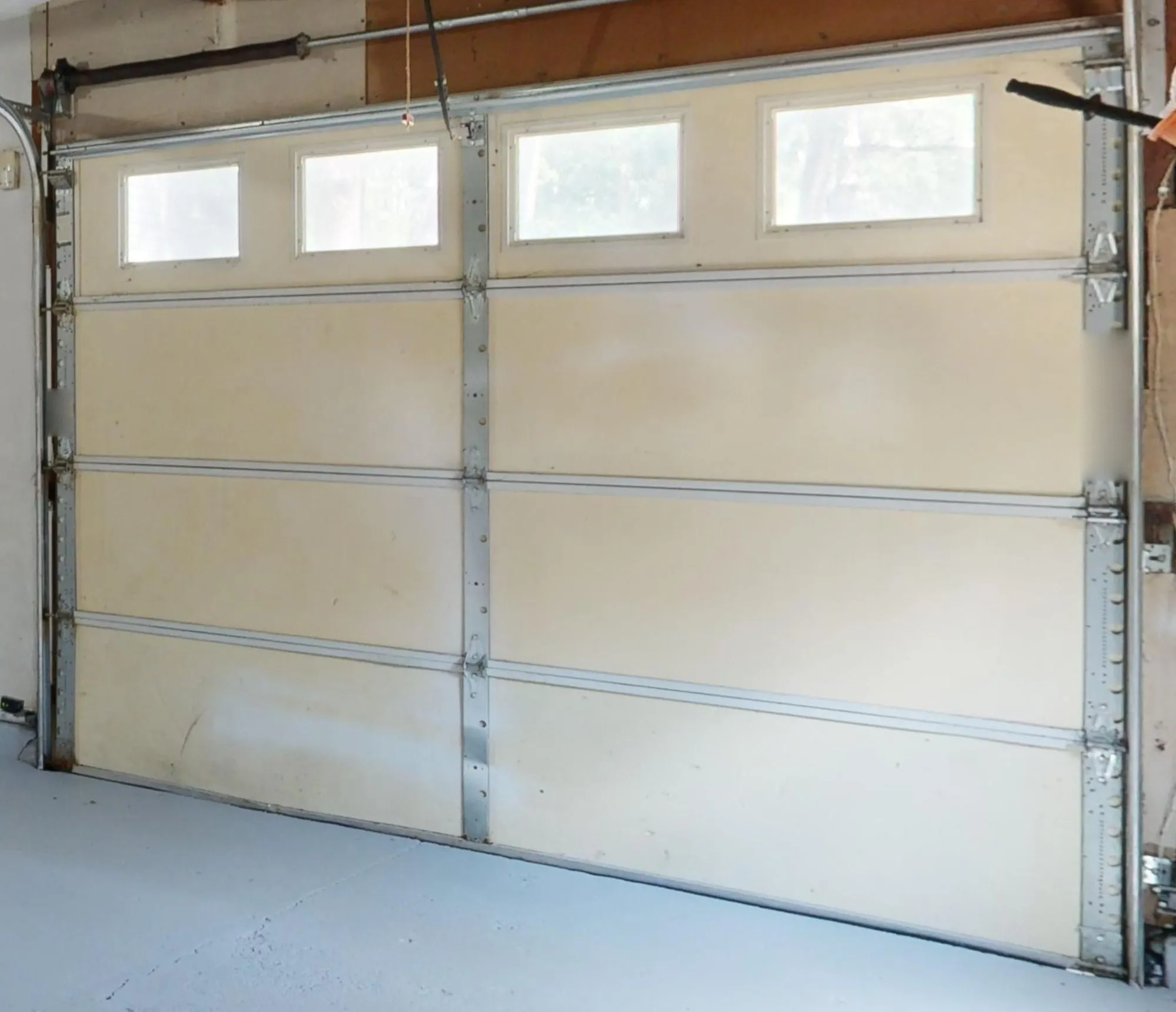 A cream sectional door seen from inside the garage, with its side tracks, hinges and the spring shaft running above it