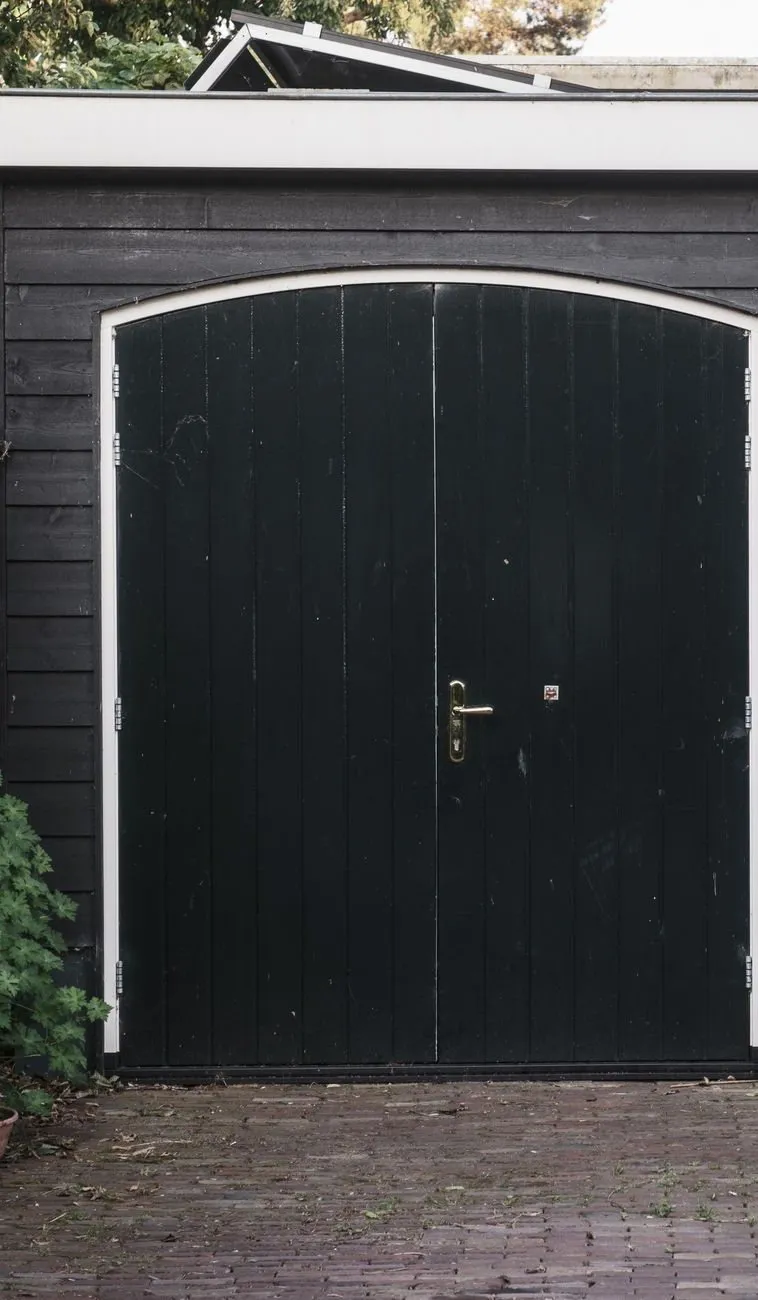 A pair of black arched timber side-hinged garage doors