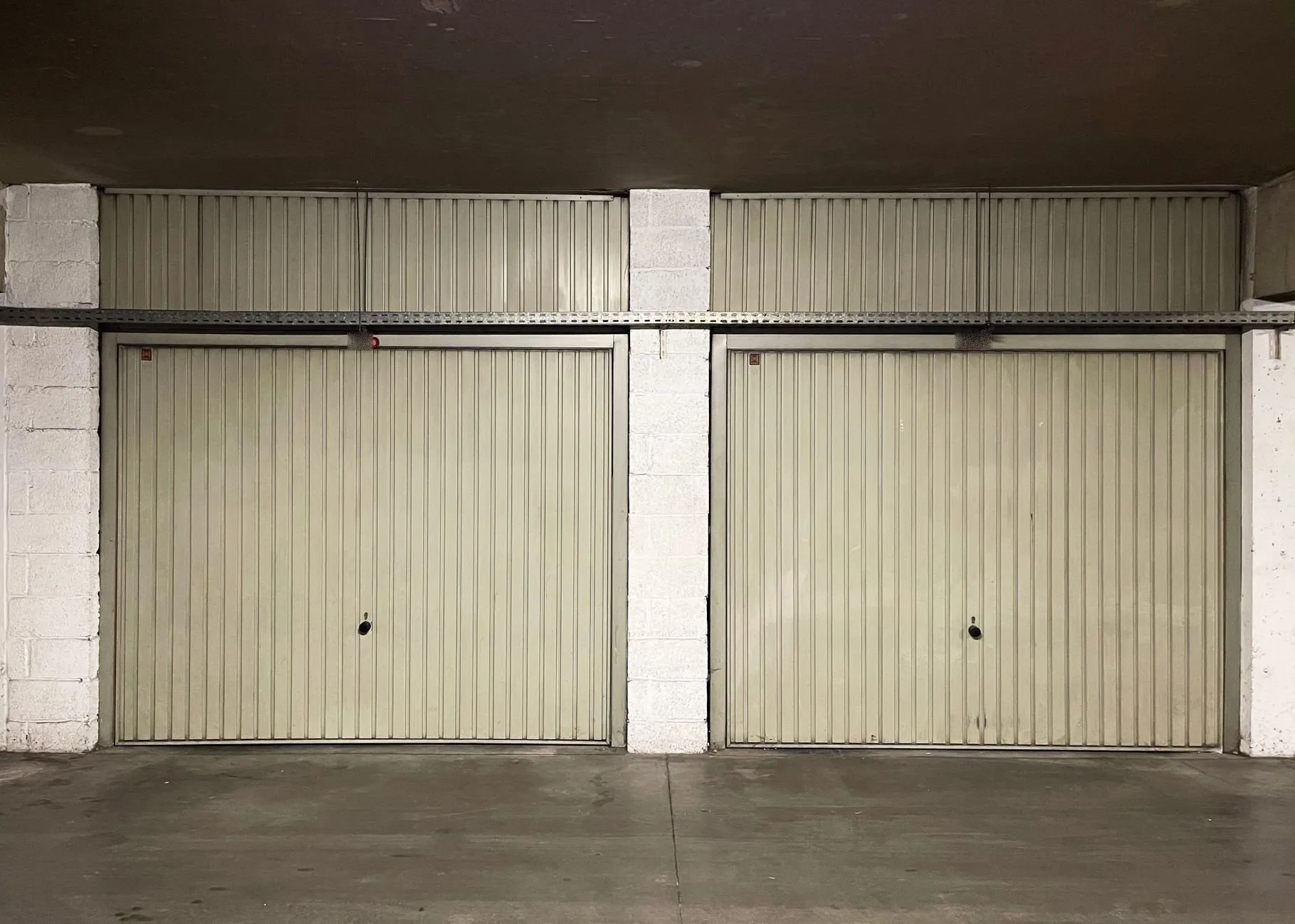 A pair of beige steel up-and-over doors in a covered garage block