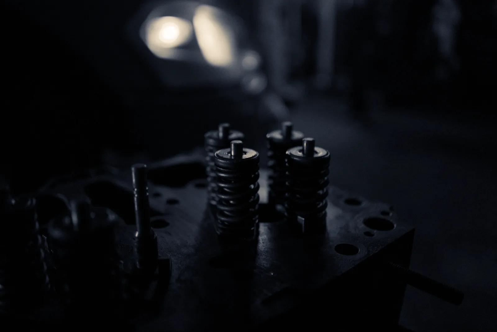 Coil springs under load on a machined plate, lit in cold steel light with a single warm highlight behind.